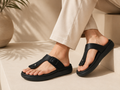 Black sandals worn with beige pants on a neutral background