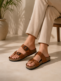 Brown sandals worn with beige pants on a neutral background