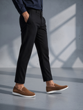 Person wearing black pants and brown shoes on a gray floor with a neutral background